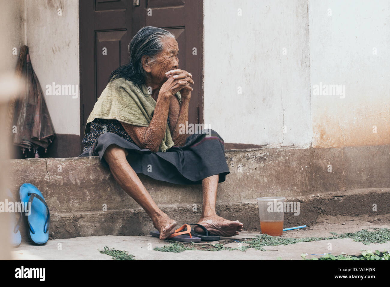 Luang Prabang, Laos - Mai 2019: alte Lao Frau sitzt auf dem Haus eine Veranda, einen nachdenklichen Blick. Stockfoto