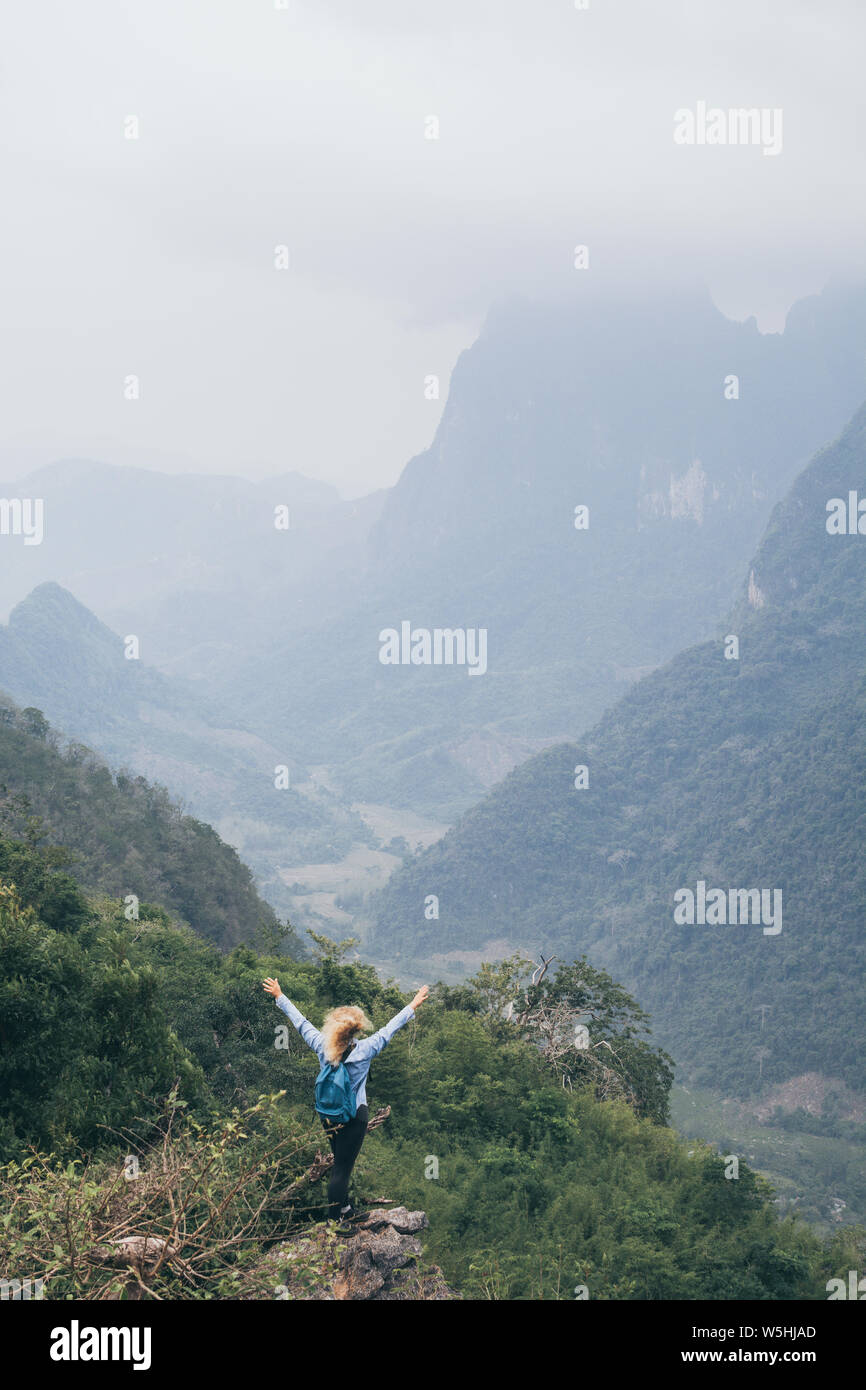 Junge kaukasier Frau steht oben auf dem Berg mit Blick auf das Flusstal in Nong Khiaw Dorf, Laos. Vertikale Ausrichtung Stockfoto Junge kaukasier Frau steht oben auf dem Berg mit Blick auf das Flusstal in Nong Khiaw Dorf, Laos. Vertikale Ausrichtung Stockfoto