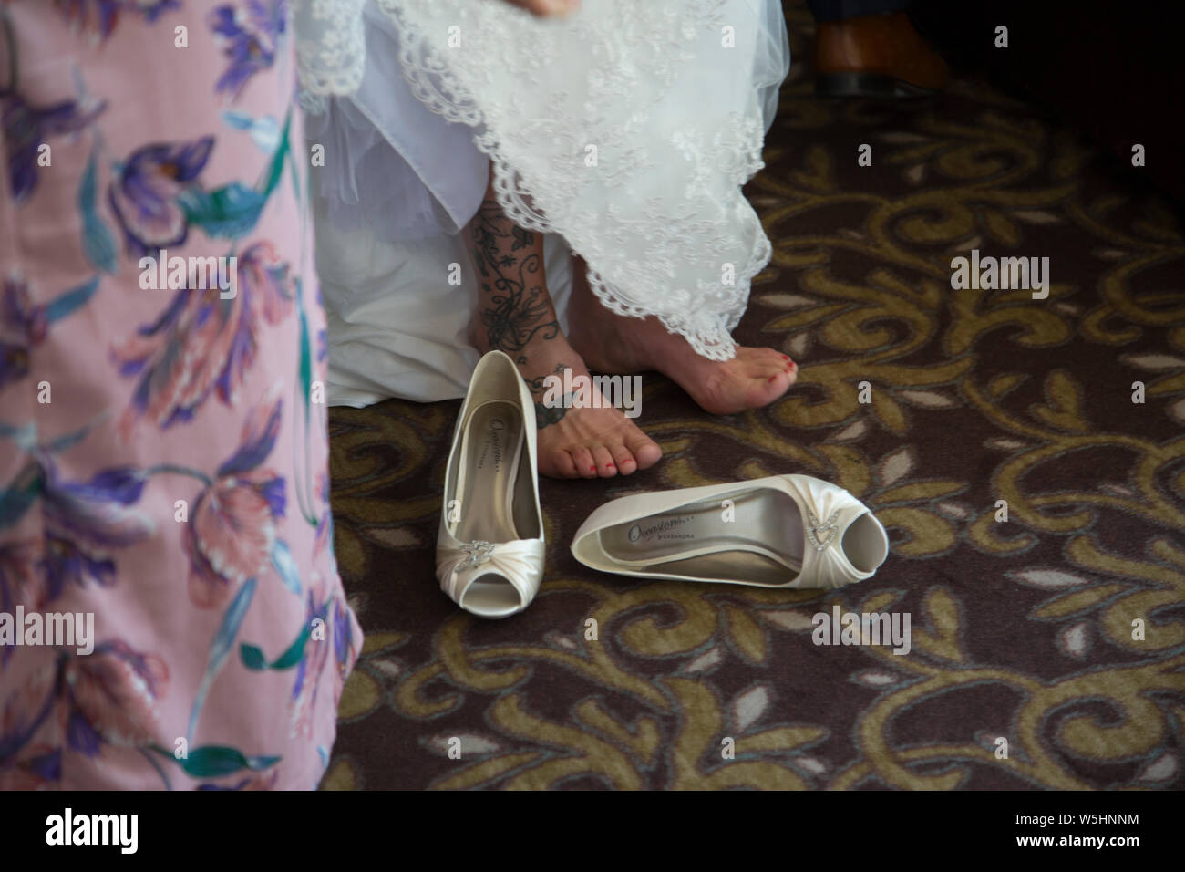 Braut ihre Schuhe ausziehen für einige Licht Relief nach ihrer Hochzeit Zeremonie Stockfoto