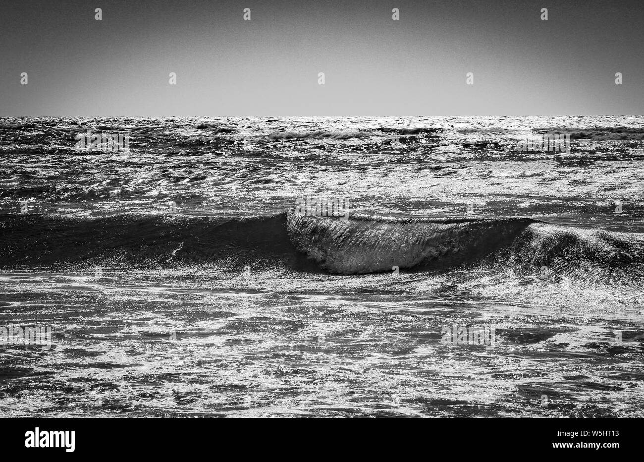 Schöne Aufnahme von Meereswellen mit klarem Himmel in der Hintergrund in schwarz und weiß Stockfoto