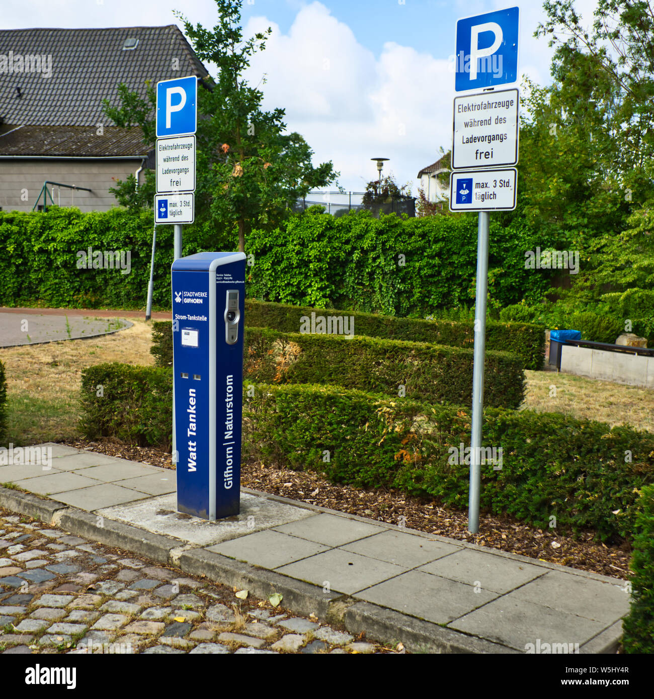 Gifhorn, Deutschland, Juli 7., 2019: Ladestation für Elektroautos auf dem Parkplatz eines kleinen Stadt, mit Hecken und Rasen im Hintergrund Stockfoto