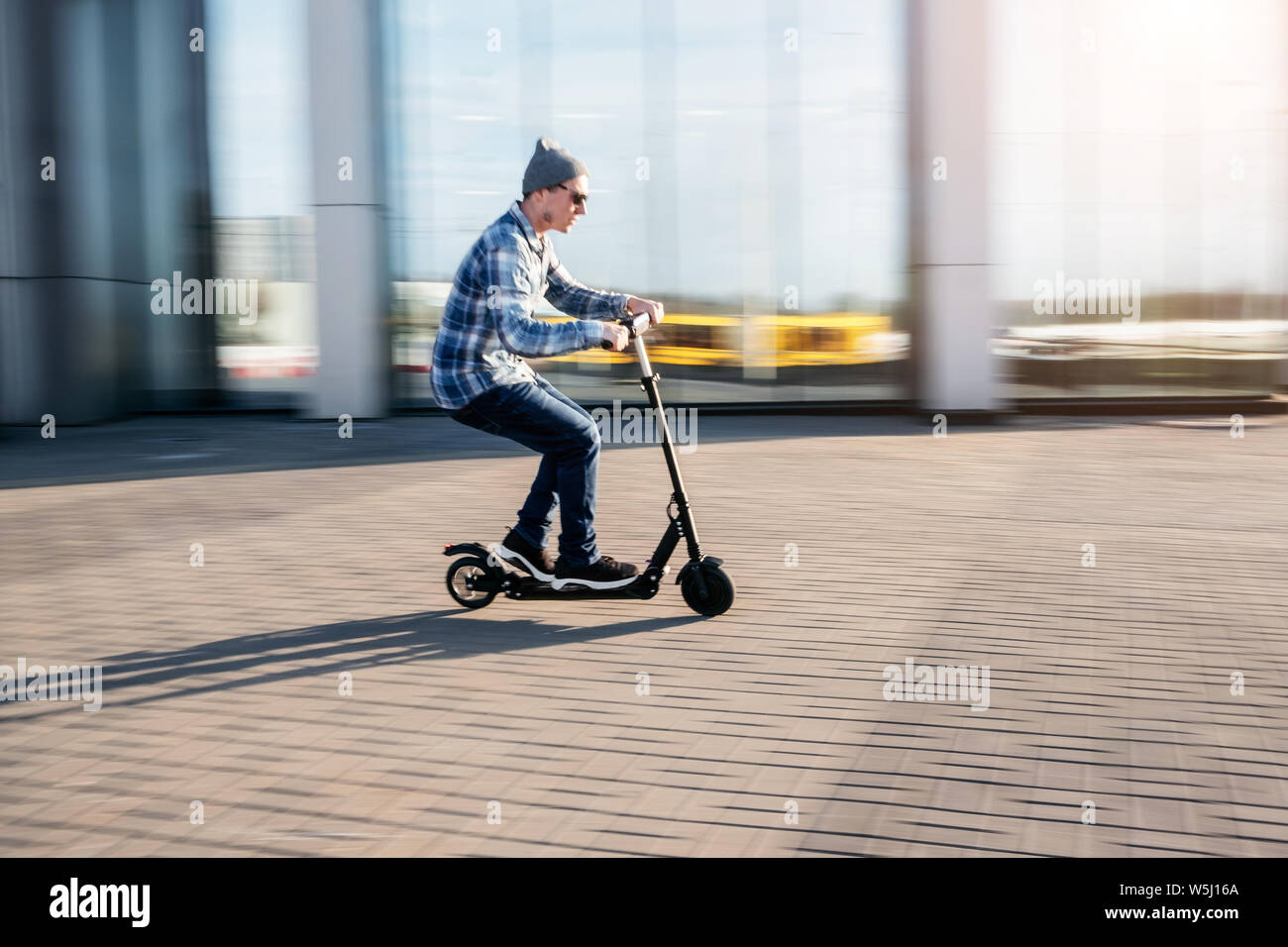 Junger Mann in Freizeitkleidung auf elektrische kick Scooter auf Stadt Straße in Bewegungsunschärfe in Sonntag Stockfoto