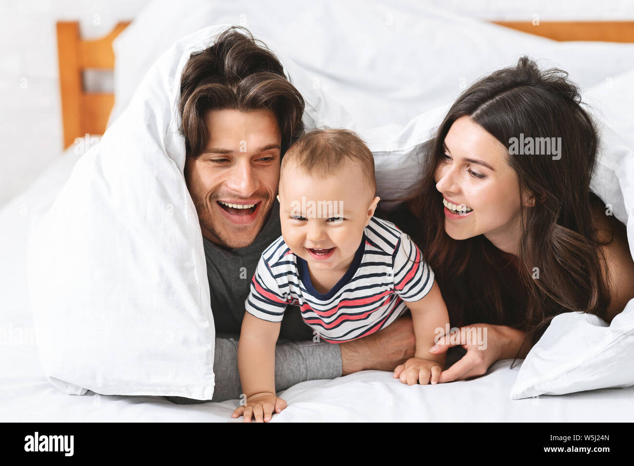 Fröhliche Eltern spielen mit Baby Sohn im Bett Stockfoto