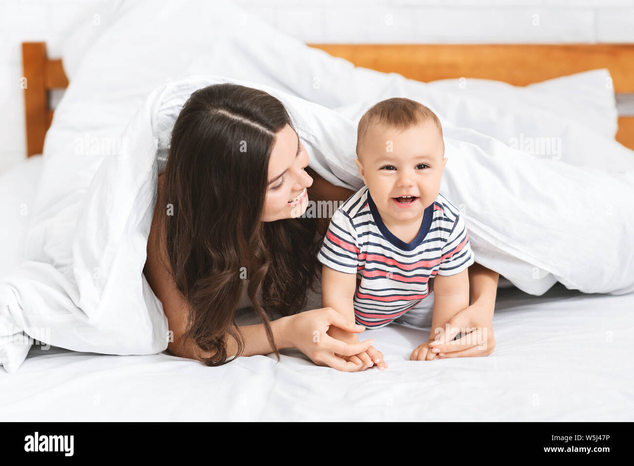 Adorable Baby krabbeln auf dem Bett, versteckt unter Decke mit Mom Stockfoto