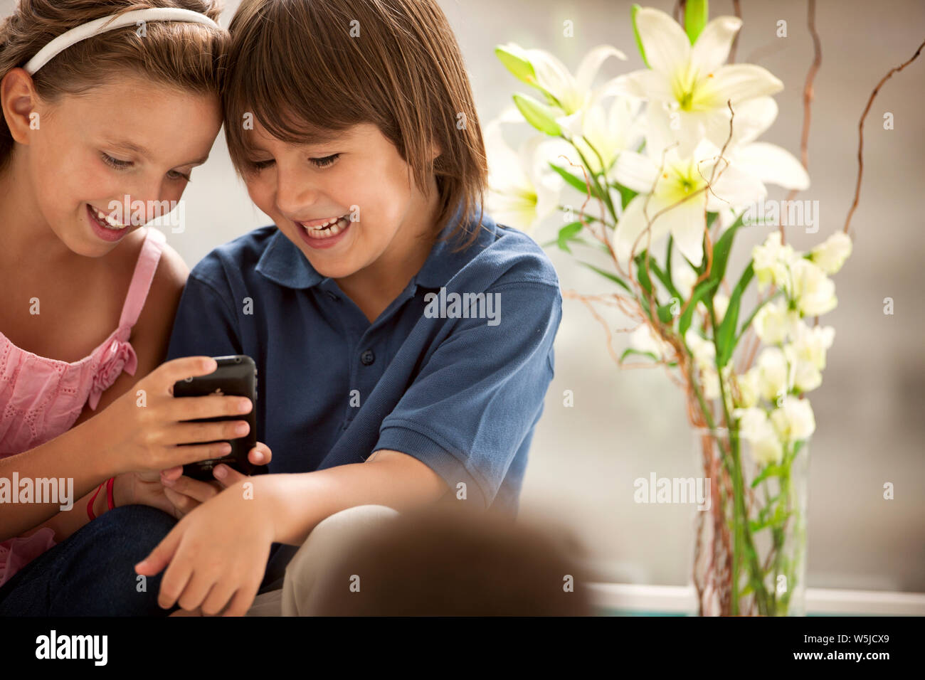 Ein Junge und ein Mädchen lächeln verschmitzt, als sie schauen auf ein Handy. Stockfoto