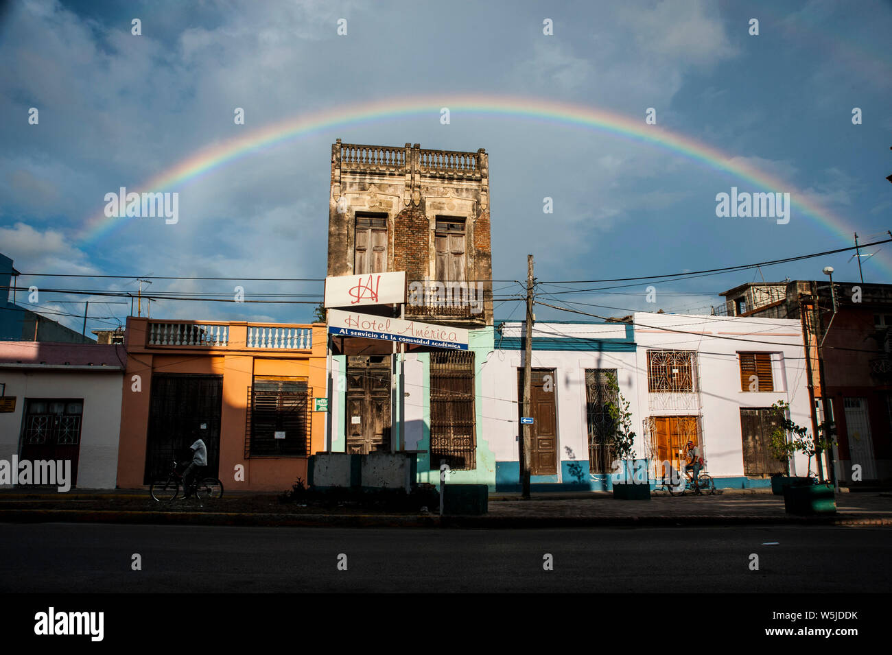 Ein Regenbogen über dem Hotel America in Camguey, Kuba wie Männer fahren mit dem Fahrrad nach einem Regenschauer Stockfoto