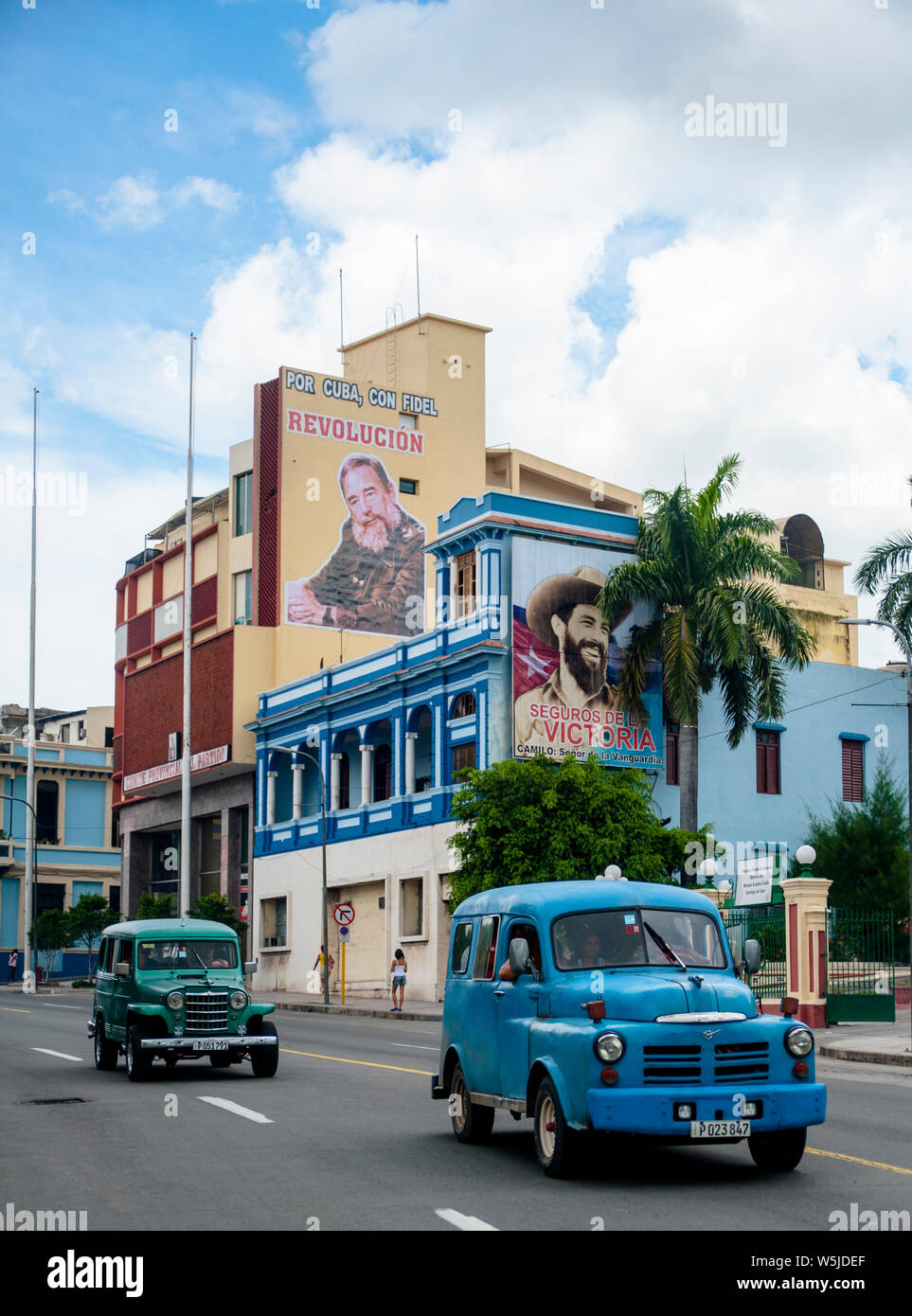 Zwei klassische Van - wie Jeeps fahren die Straßen von Santiago de Cuba Vergangenheit Wandmalereien von Fidel Castro und Camilo Cienfuegos Stockfoto