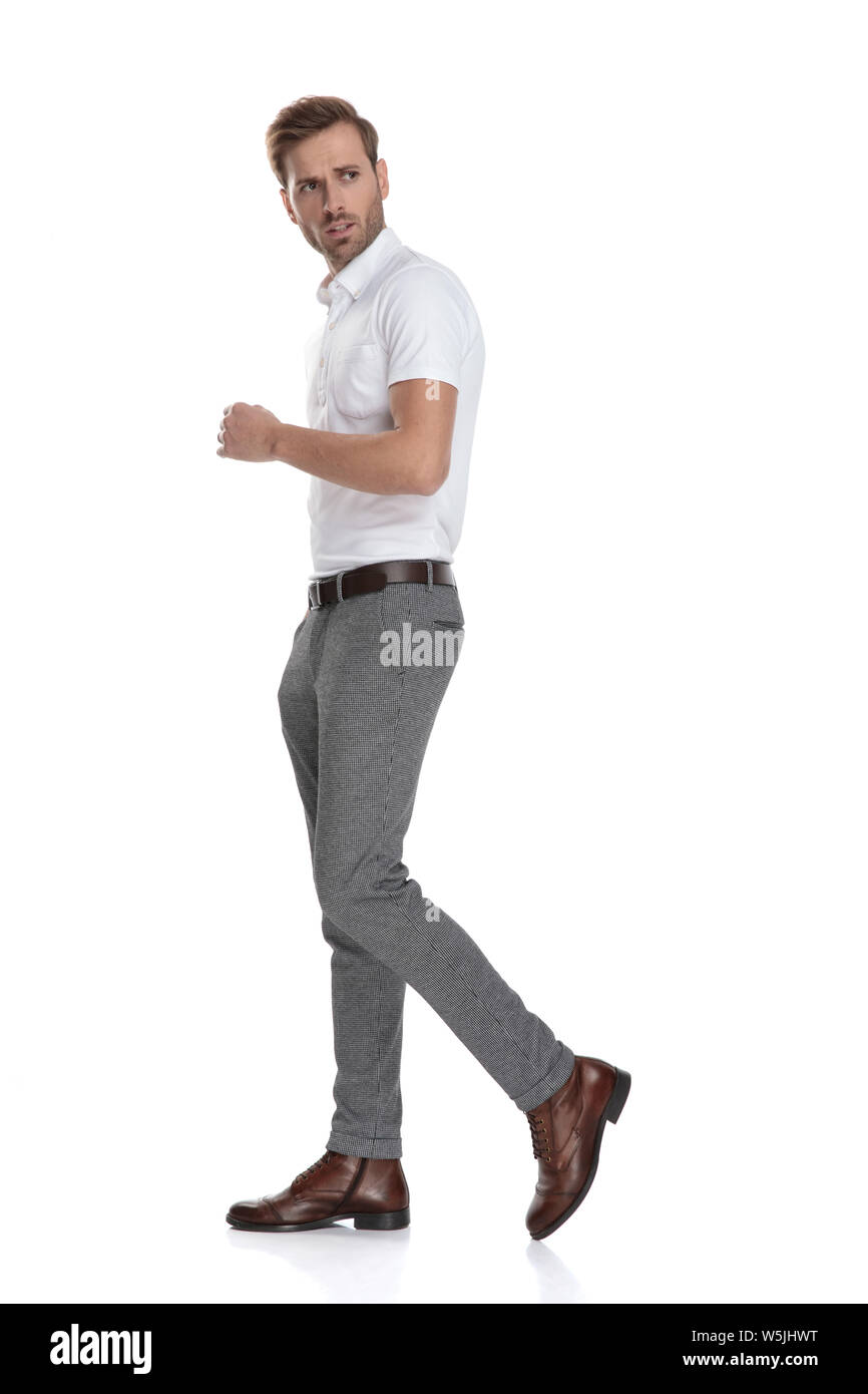 Ernsthafte junge legerer Mann Spaziergänge und blickt über die Schulter ein wenig besorgt auf weißem Hintergrund Stockfoto