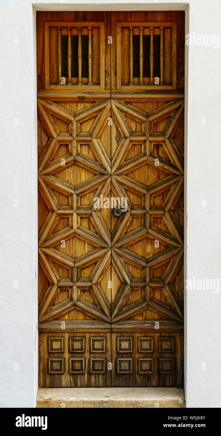 Verwitterte braune Holztür mit kunstvollen Schnitzereien in Weiß Türrahmen (vertikale Ausrichtung im Hochformat) Stockfoto