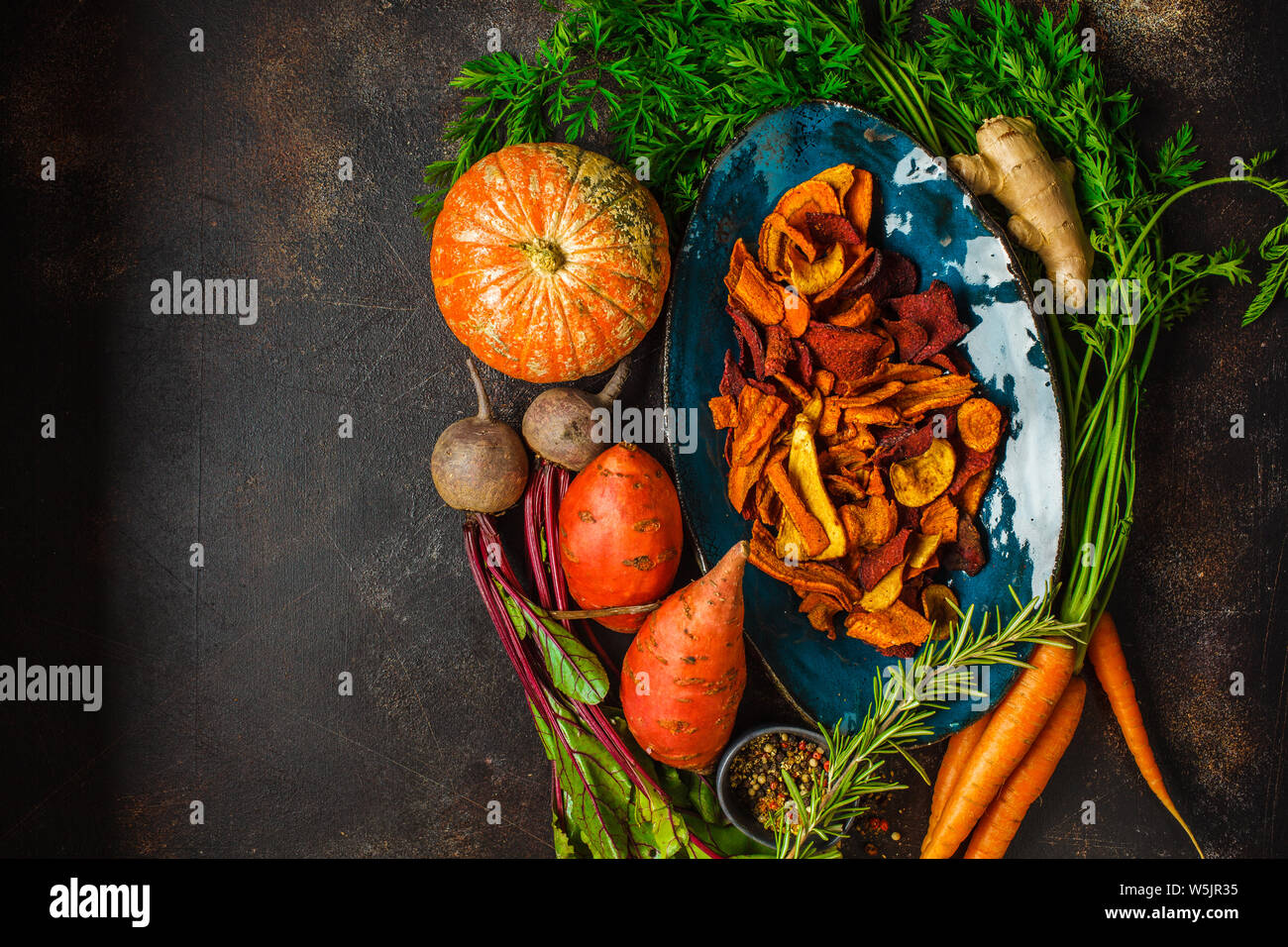 Schüssel, gesunde Gemüse Chips aus Rüben, süsse Kartoffeln und Karotten mit Zutaten auf dunklem Hintergrund, Ansicht von oben. Stockfoto