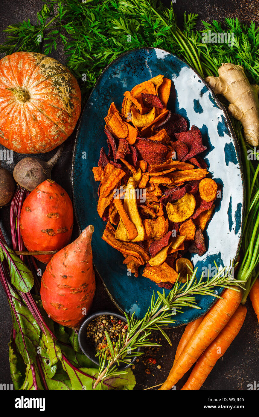 Schüssel, gesunde Gemüse Chips aus Rüben, süsse Kartoffeln und Karotten mit Zutaten auf dunklem Hintergrund, Ansicht von oben. Stockfoto