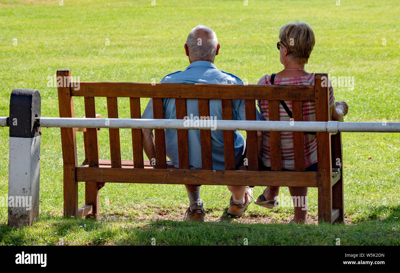 Ein älteres Ehepaar genießen Sie eine ruhige Zeit auf einer Parkbank in Broadway, Worcestershire, England, Großbritannien Stockfoto