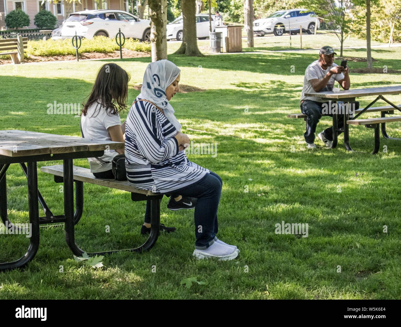 Shoeless, eine muslimische Frau betet im Park unter den gleichgültigen Augen des Anderen. Stockfoto