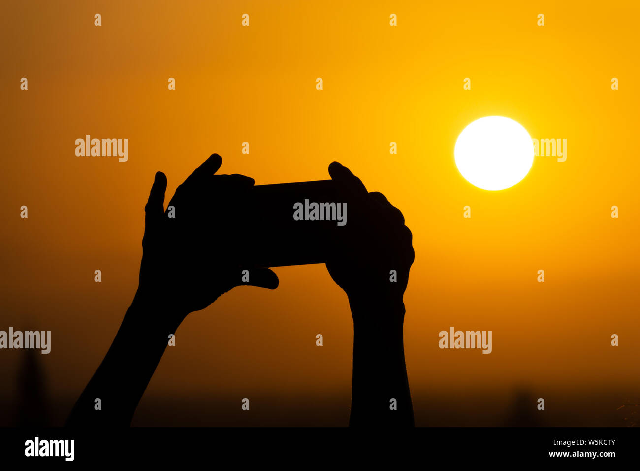 Silhouette der Hände halten ein Handy und die Fotografie des riesigen Sonne bei Sonnenuntergang oder Sunrise. Männliche macht ein Foto auf seinem Telefon Stockfoto