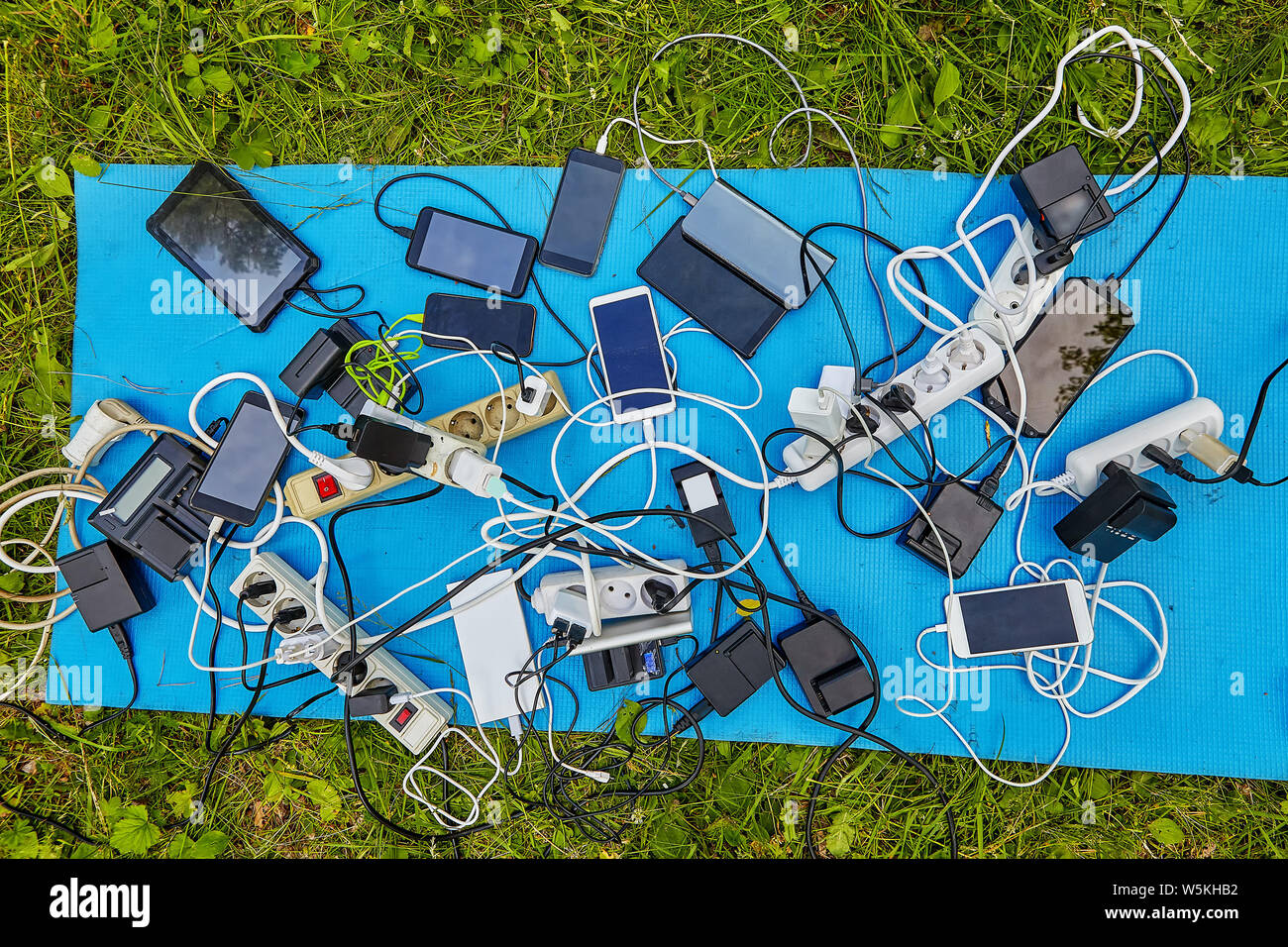 Eine Menge Batterien, Ladegeräte für Smartphones und elektrische Verlängerungskabel mit elektrischen Geräten, Bildschirme, die von ihnen in Rechnung, sie liegen auf Stockfoto