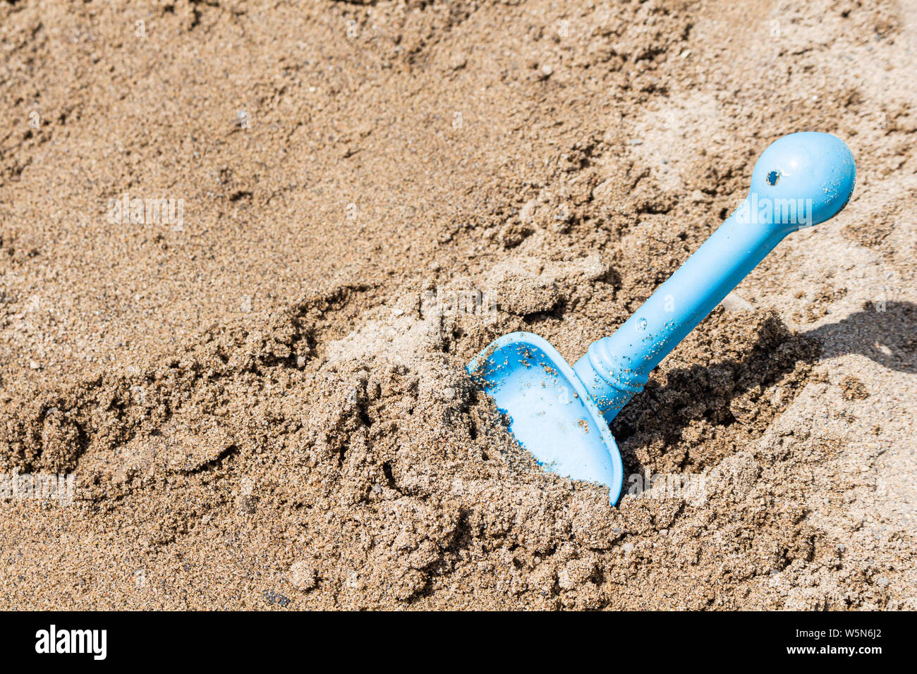 Eine blaue Spielzeug Schaufel ist in den Sand an einem sonnigen Strand im Sommer geschoben. Stockfoto