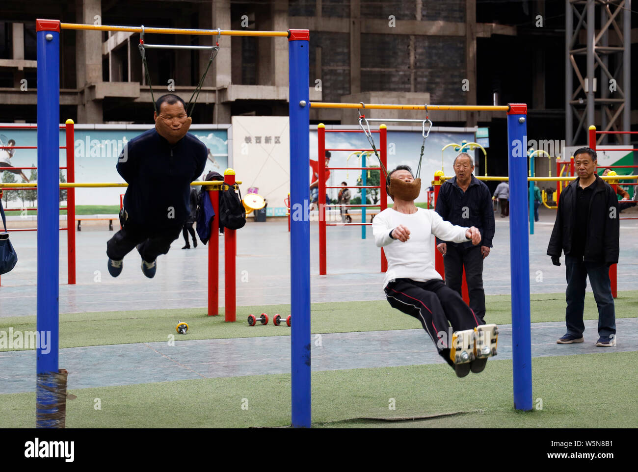 Der 57-jährige Chinese Sun Rongchun, Links, und ein anderer Mann Übung mit improvisierten zervikalen Traktion Geräte zu hohen Bars beim Sport beigefügt kompl Stockfoto