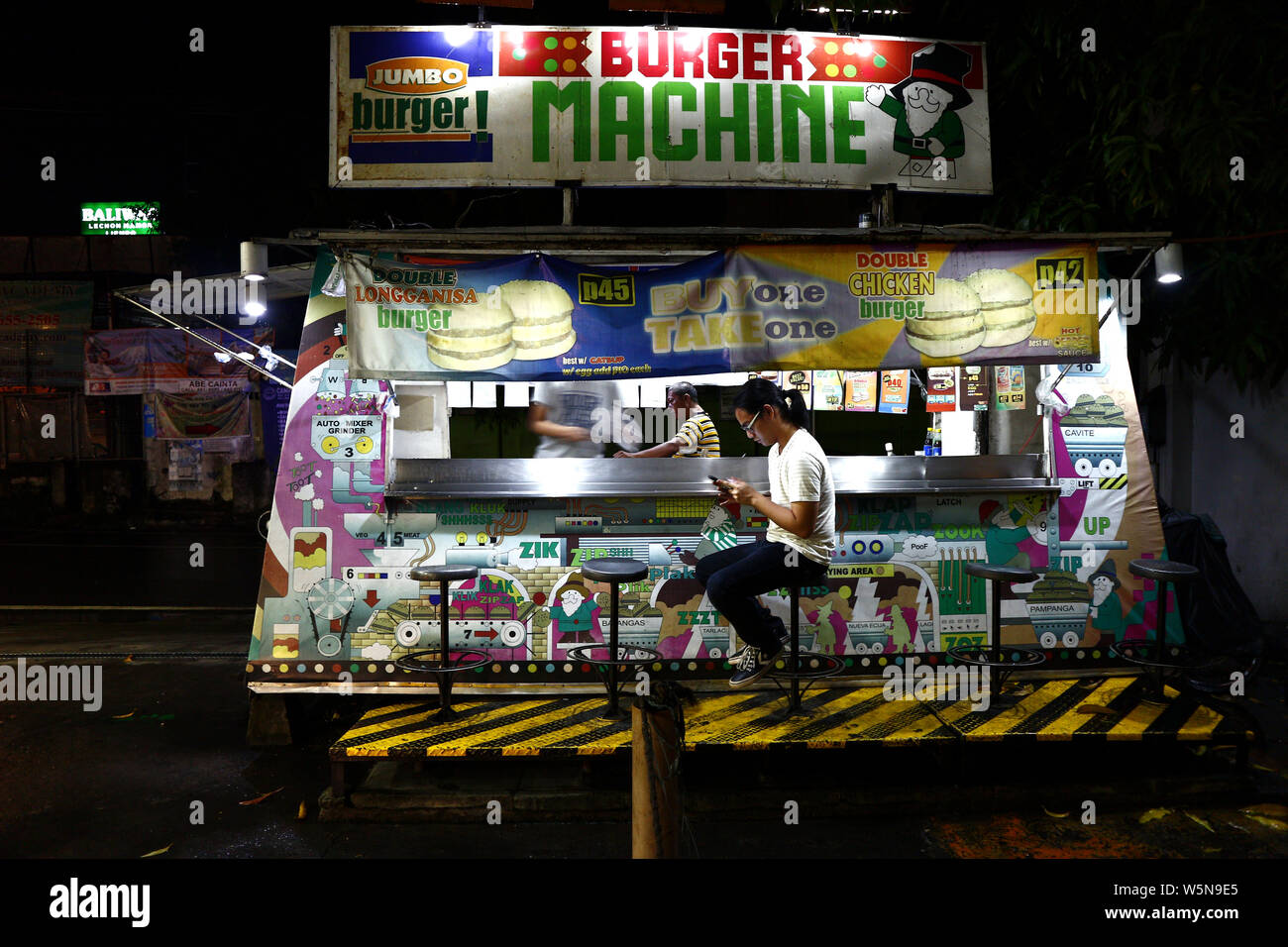TAYTAY, Rizal, Philippinen - Juli 27, 2019: ein Kunde an einem Hamburger Stall mit seinem Smartphone während des Wartens auf sein Essen. Stockfoto