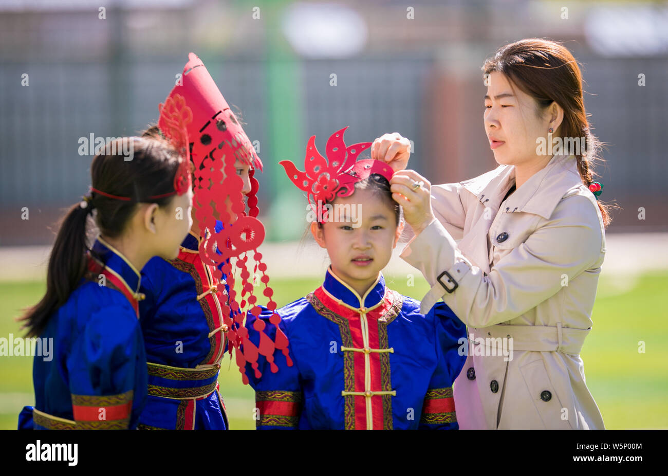 Chinesische primäre Studenten in traditionellen Kostümen gekleidet und tragen Papier schneiden headwears an einer Schule in der Stadt Huhhot darstellen, Norden Chinas Stockfoto