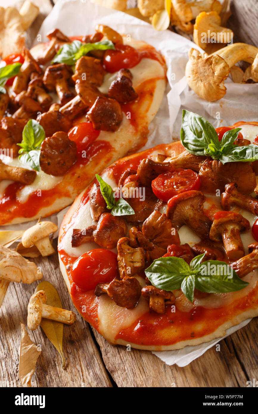 Hausgemachte saftige Pizza mit Pfifferlingen, Mozzarella, Tomaten und Basilikum close-up auf Pergament auf den Tisch. Vertikale Stockfoto