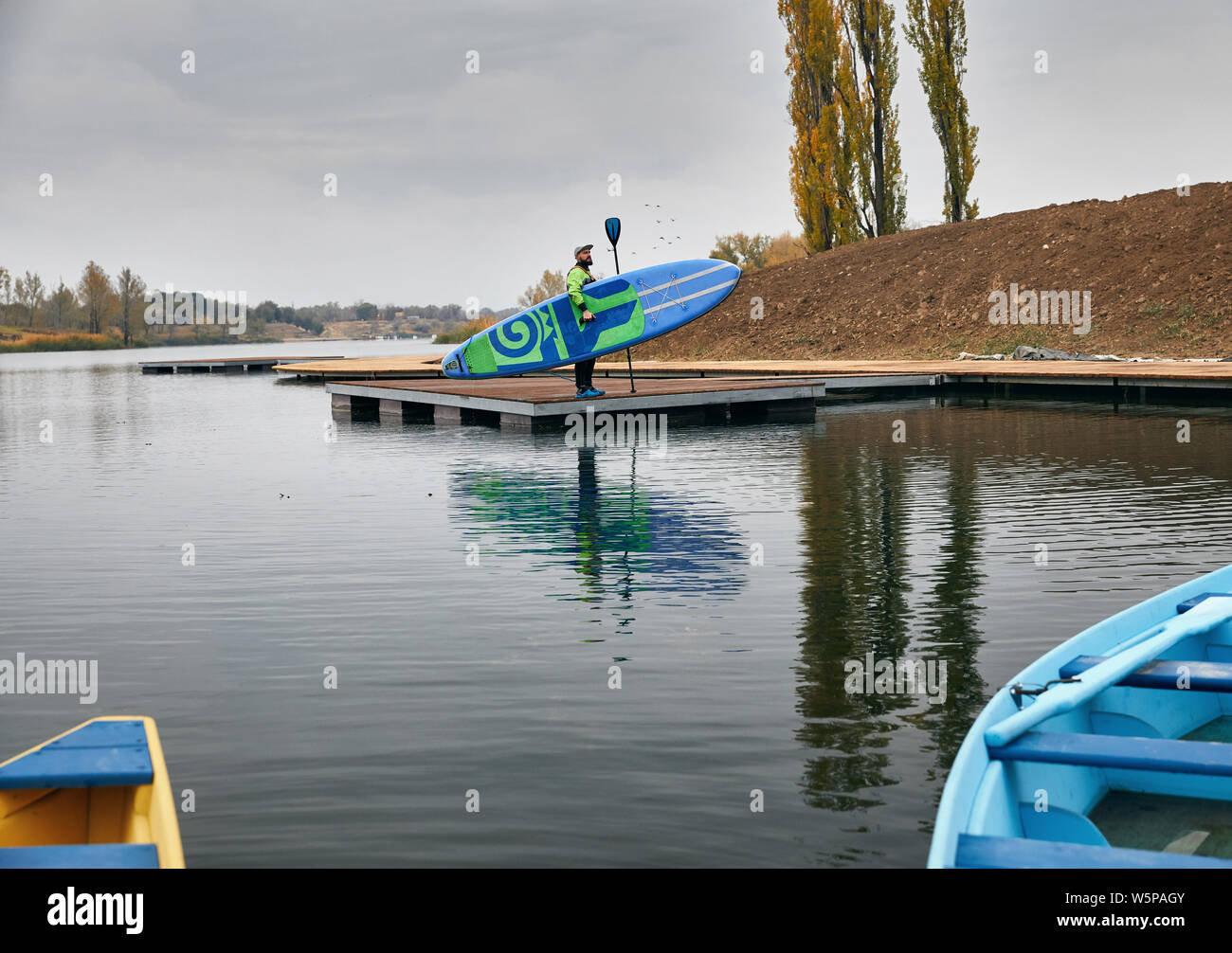 Bärtiger Mann im Neoprenanzug holding Surfbrett und Paddeln am See Pier Stockfoto