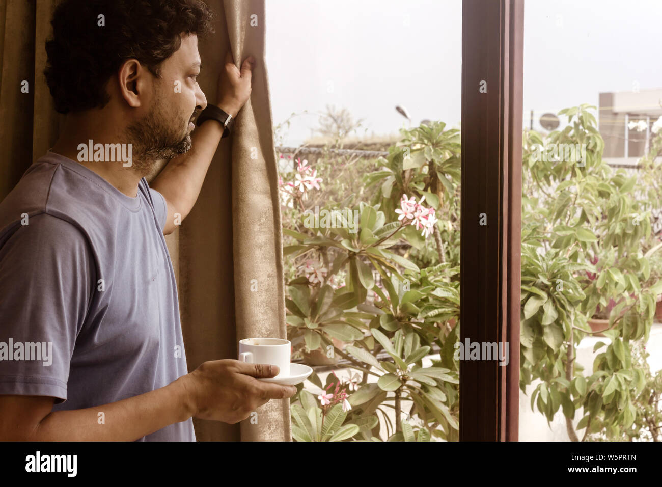 Mann hält eine leckere Tasse duftende Kaffee am Morgen, entspannend und schauen durch das Fenster. Morgensonne Licht von außerhalb kommen. Happy Weekend Stockfoto