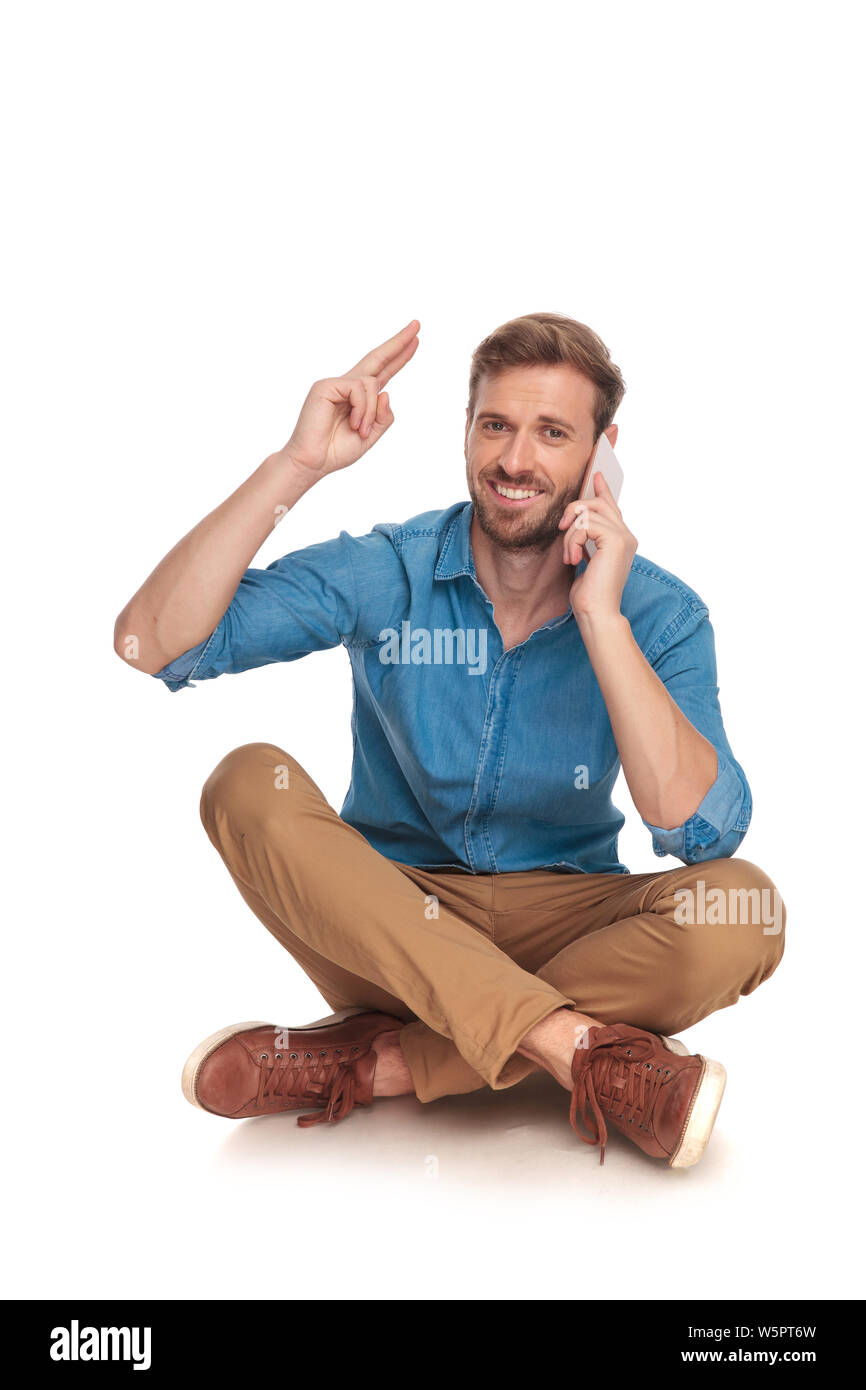 Gerne sitzt legerer Mann telefoniert und grüßt alle mit einem militärischen Gruß mit den Fingern auf weißem Hintergrund zur Stirn Stockfoto