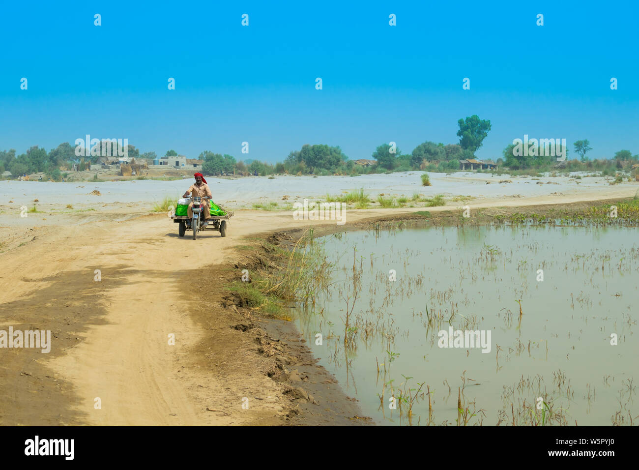 Punjab, Pakistan-June 23,2019: Ein unbekannter Mann ein moto Rikscha in einer Flut betroffenen Bereich, blauer Himmel. Stockfoto