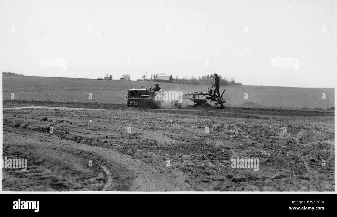 Mechanisierte Straße - Einstufung in die Besoldungsgruppe. Des Lacs NWR, North Dakota; Umfang und Inhalt: Eine kleine Planierraupe Ziehen einer Reiten in eine riesige Fläche von offenen Felder pflügen, mit landwirtschaftlichen Gebäuden und Kulturen im Hintergrund. Stockfoto