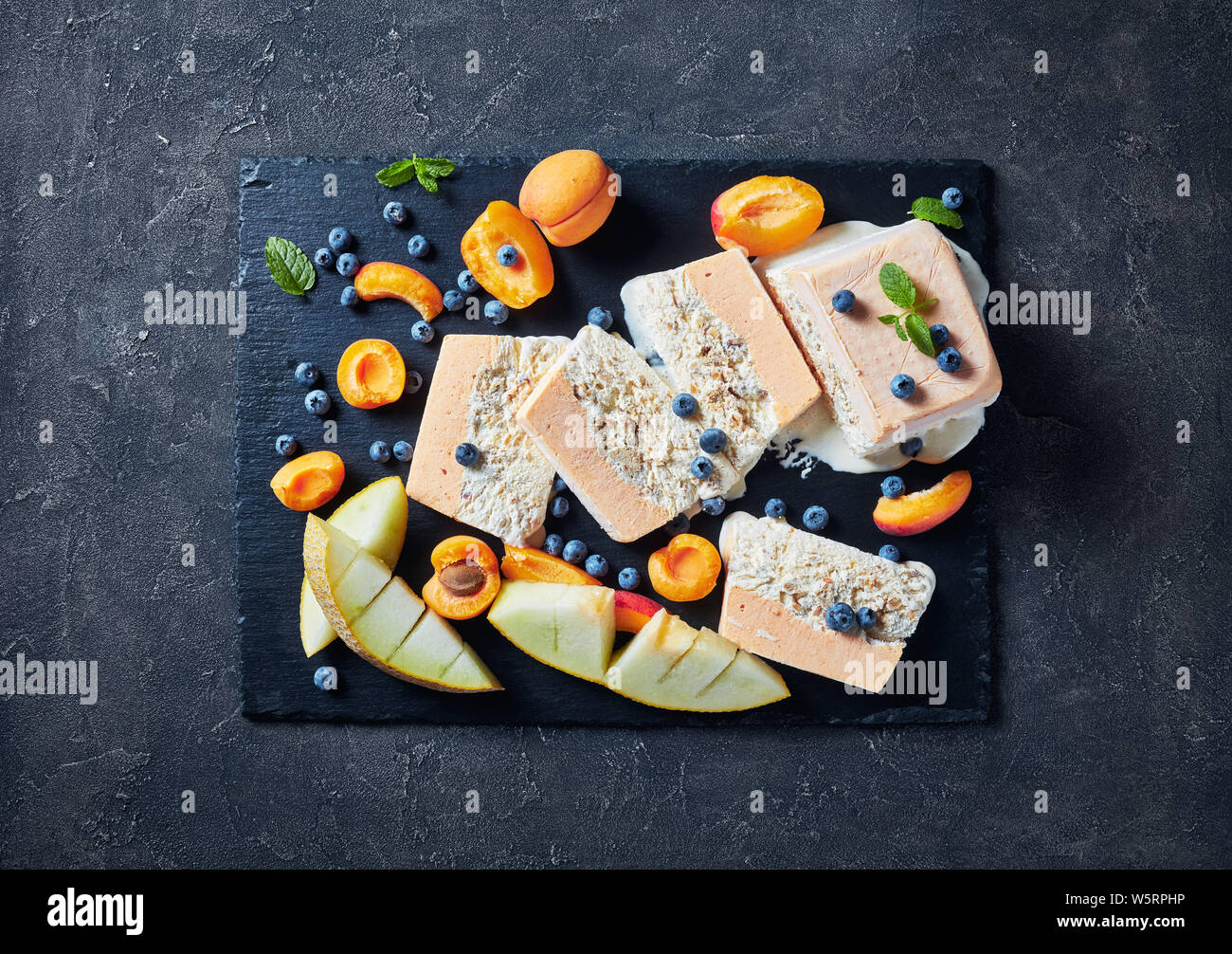 In der Nähe von Schmelz Semifreddo alle Mandorle, sizilianischen Mandeln Semifreddo mit Aprikose und Melone in Scheiben geschnitten auf einer Schiefertafel Teller mit Früchten und Beeren, Anzeigen Stockfoto