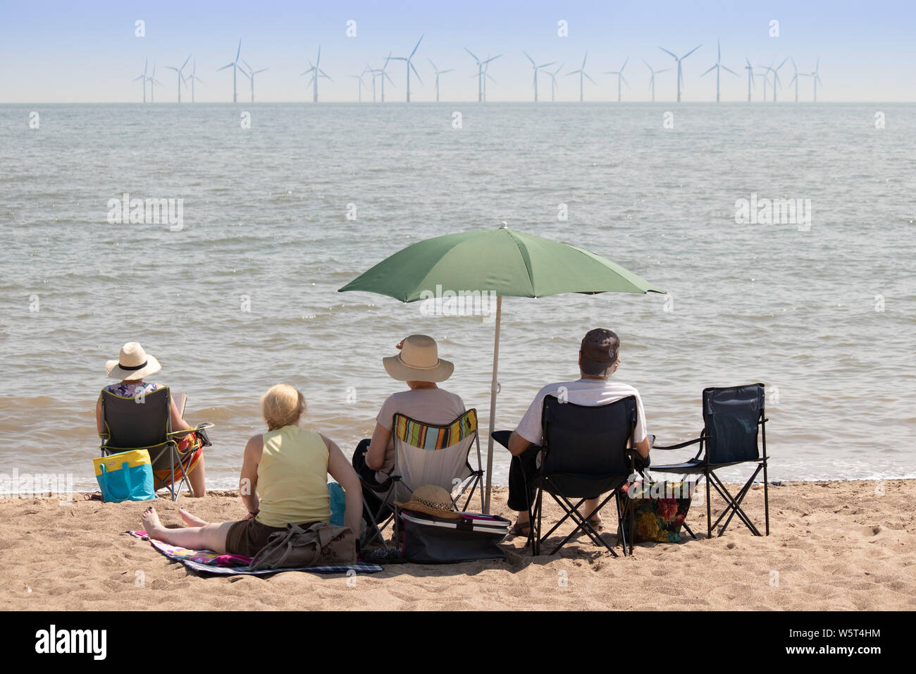 Warmes Wetter in Skegness. Die Leute am Strand mit Blick auf die Windkraftanlagen vor der Küste Stockfoto