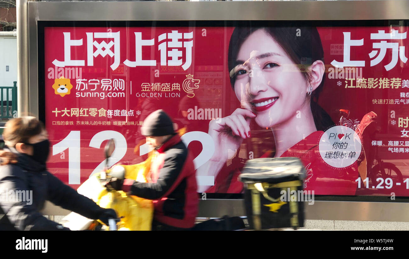 ---- Radfahrer fahren an eine Werbung für Chinesische Elektronikfachhändler Suning Holdings Group mit Schauspielerin Jiang Shuying auf einer Bushaltestelle in Sein Stockfoto
