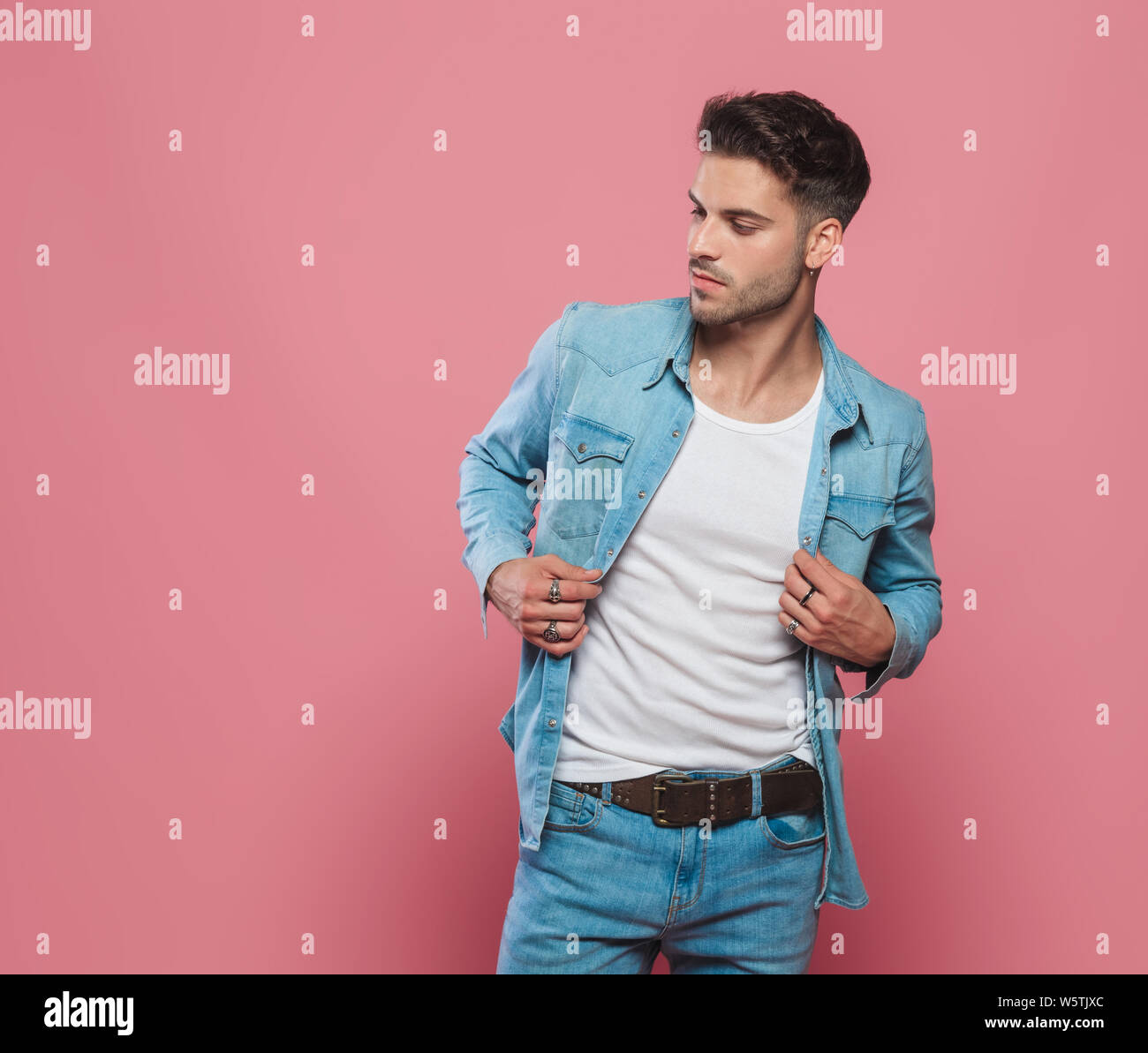 Portrait des jungen Mannes holding Kragen seines Jeanshemd und Suchen auf die Seite beim Stehen auf rotem Hintergrund Stockfoto