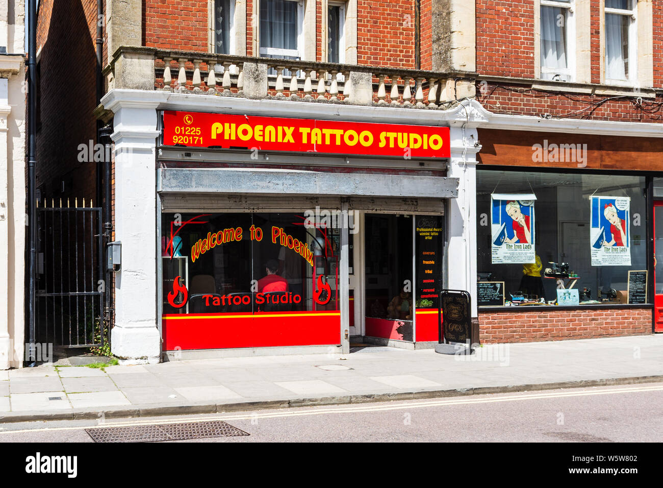 Das vordere Fenster des Phoenix tattoo studio Shop in Chippenham Wiltshire mit dem Kopf und Rücken von jemand im Wartebereich sitzen sichtbar Stockfoto
