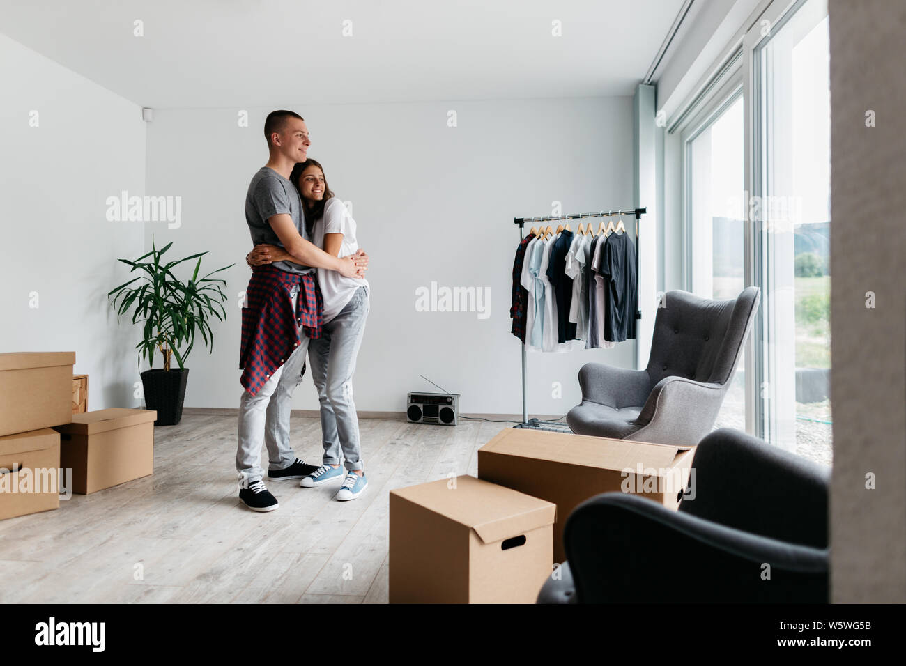 Glückliches Paar umarmen zusammen im neuen Haus. In zusammen - junge fröhliche Mann und Frau kuscheln im Zimmer mit Kartons. Stockfoto
