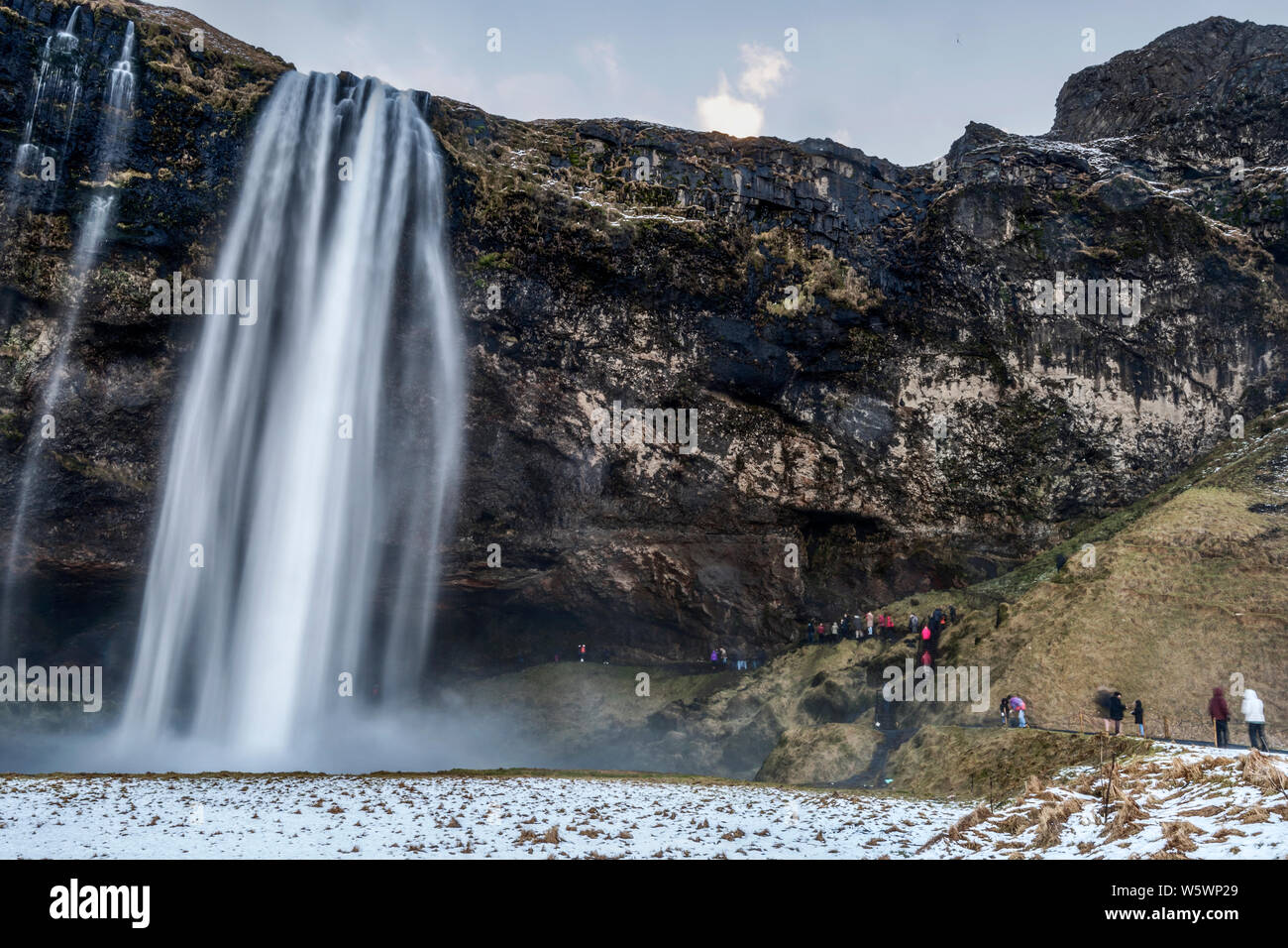Touristen, kaltes Wasser Brise aus Seljalandsfos Wasserfall im Winter in Island Stockfoto