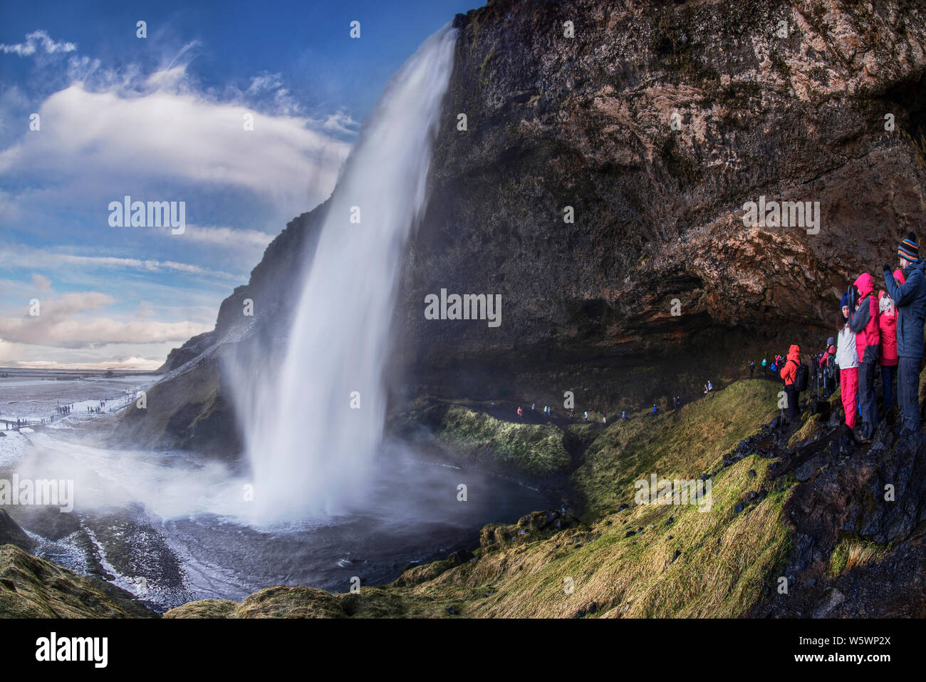 Touristen, kaltes Wasser Brise aus Seljalandsfos Wasserfall im Winter in Island Stockfoto