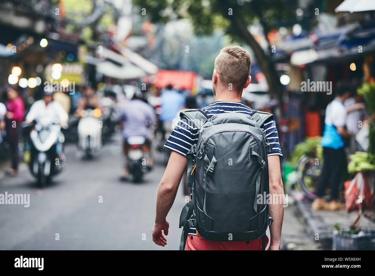 Reisenden zu Fuß auf der belebten Straße der Stadt. Ansicht der Rückseite des jungen Mann mit Rucksack im alten Viertel von Hanoi, Vietnam. Stockfoto