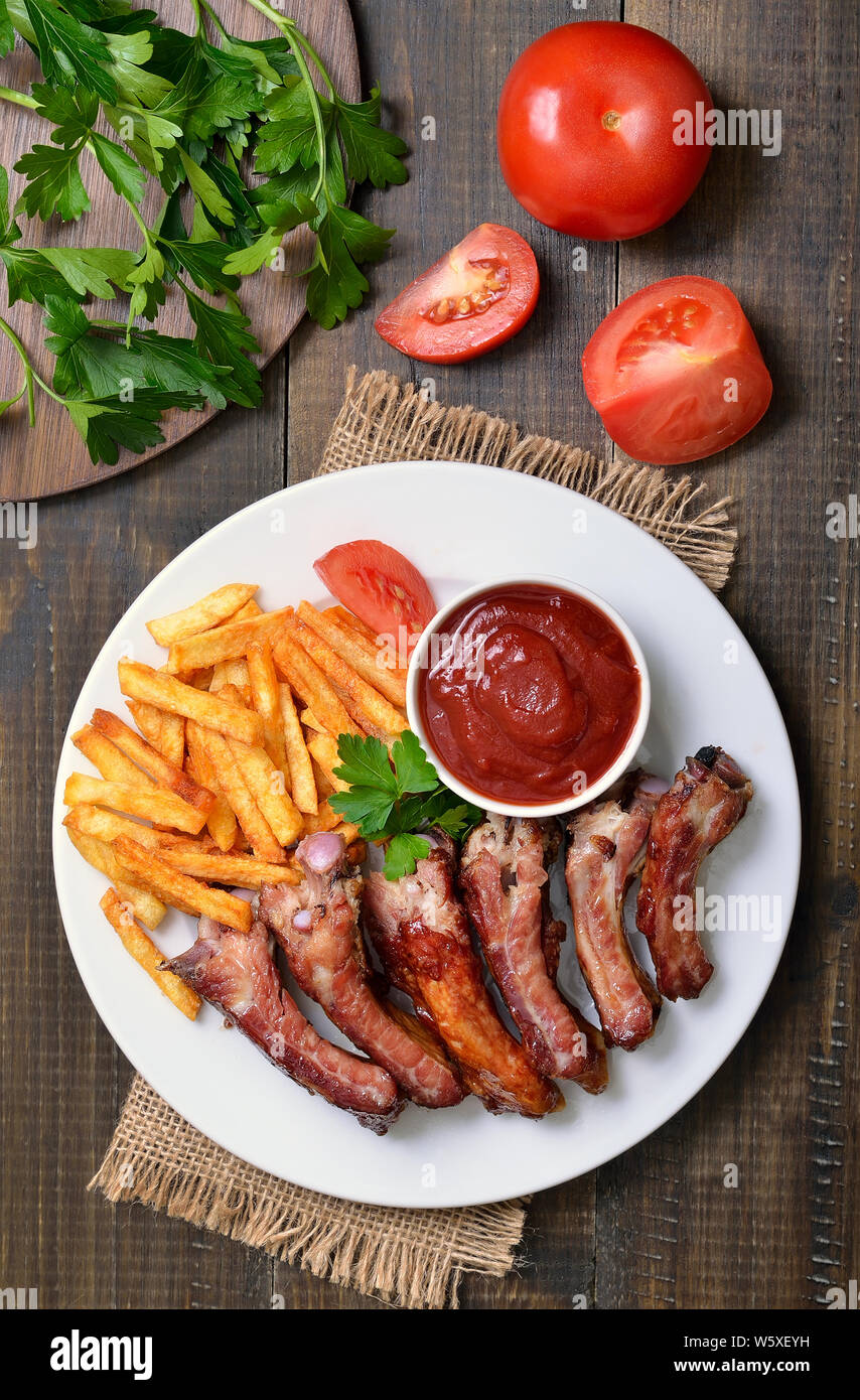 Gegrillte Schweinerippchen, Gemüse, Kartoffel, Pommes und Tomatensauce auf Holztisch, Ansicht von oben Stockfoto