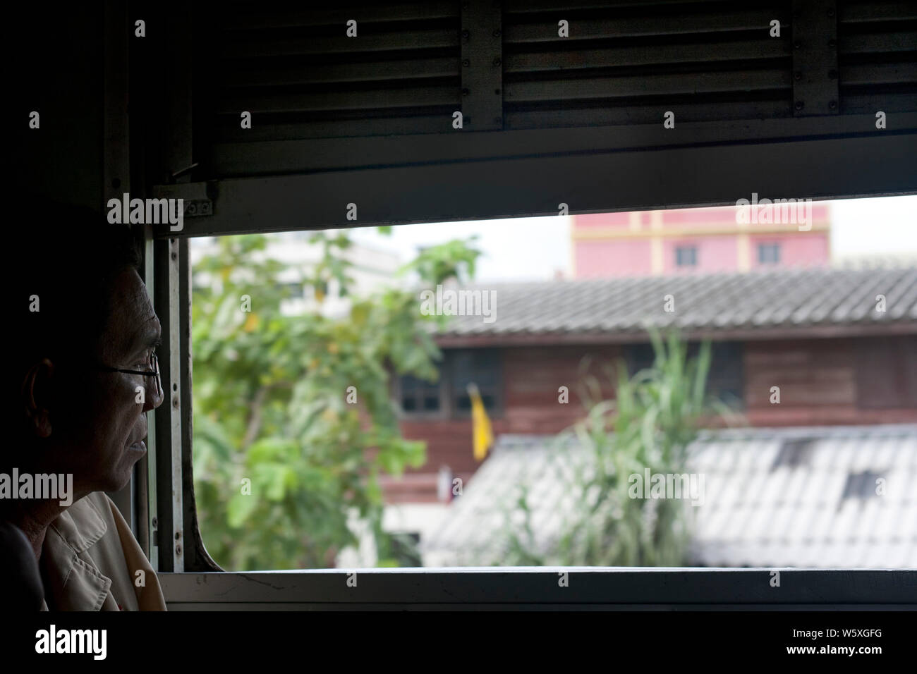 Elder thailandese Mann schaut durch ein Fenster auf einen Bahnhof in Bangkok, Thailand. Stockfoto