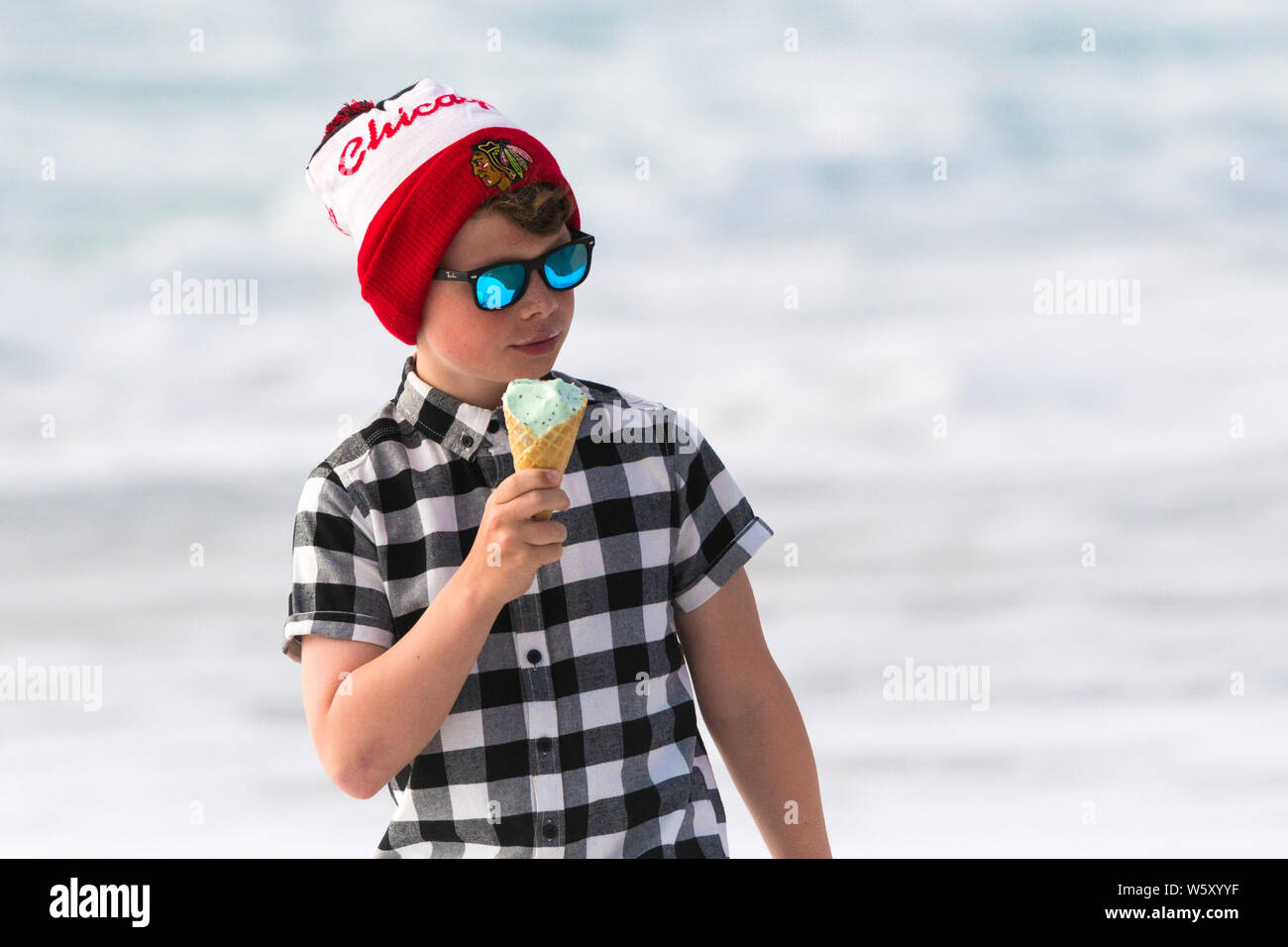 Ein Junge das Tragen von reflektierenden Sonnenbrille, T-Shirt und ein Chicago Blackhawks bobble Hut essen ein Eis. Stockfoto