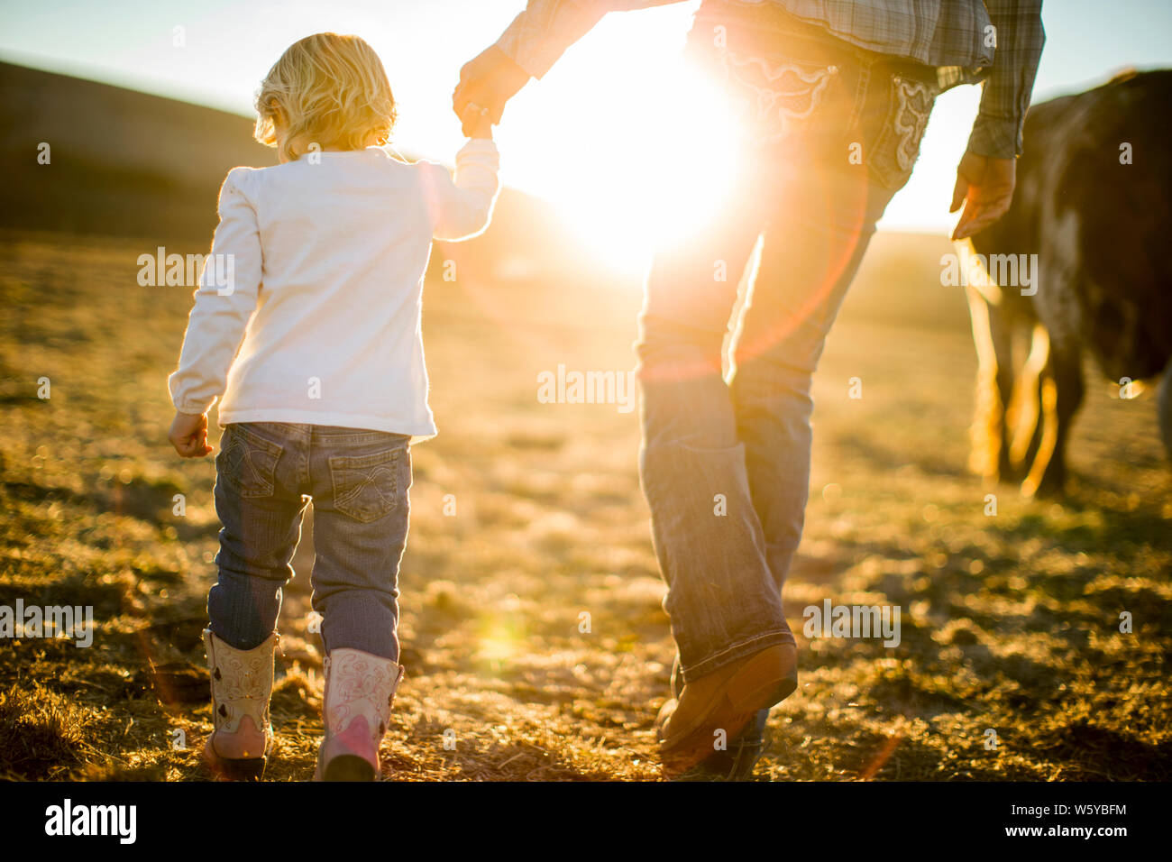 Bäuerin und ihren Toddler Tochter gehen Hand-in-Hand durch die Ranch Paddocks bei Sonnenuntergang. Stockfoto