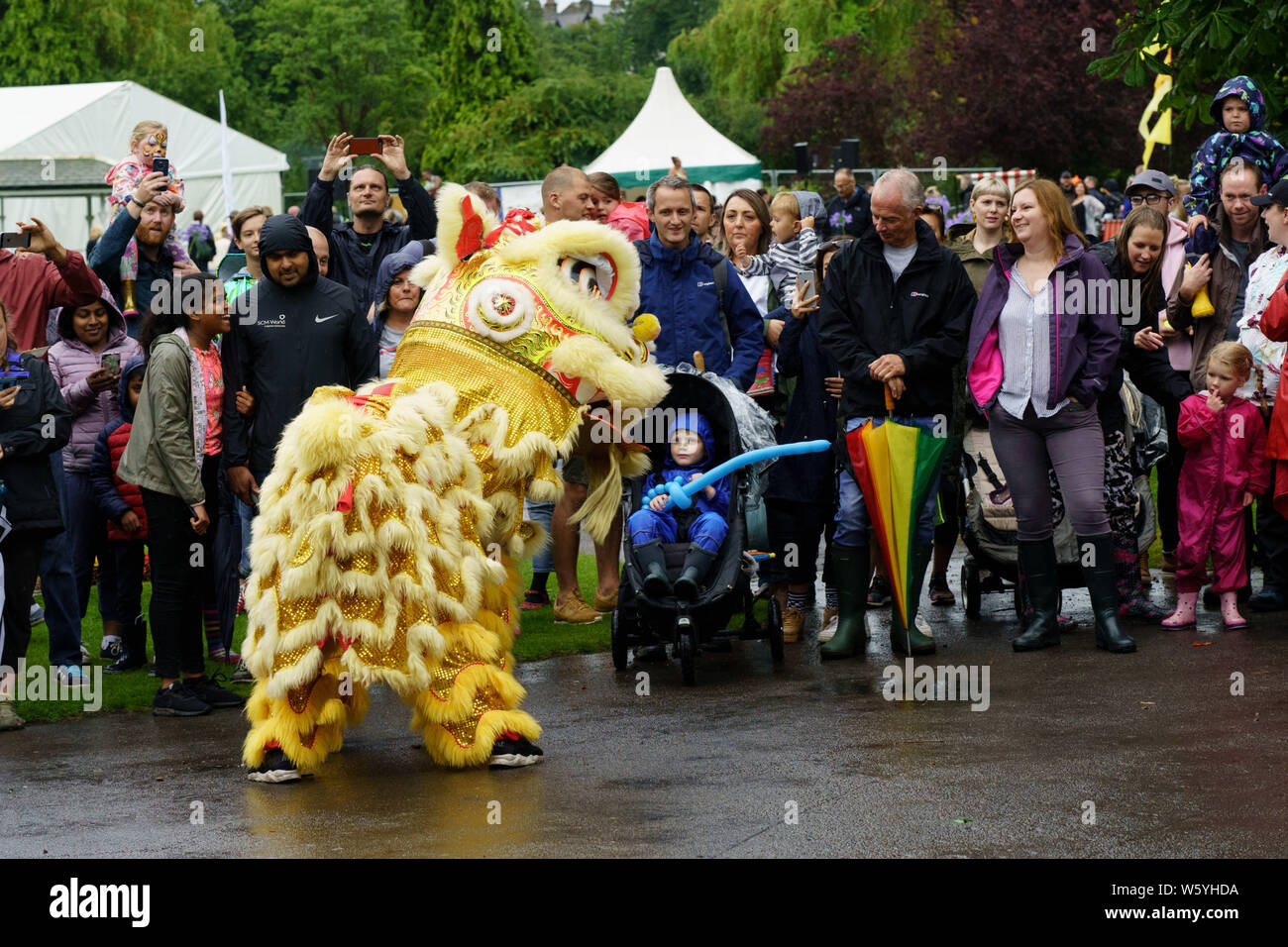 Menschen beobachten einen gelben chinesischen Drachen bei einem Karneval in den Valley Gardens, Harrogate, North Yorkshire, England, Großbritannien. Stockfoto