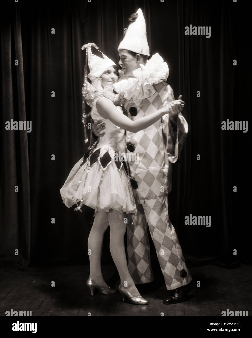 1920 LÄCHELNDE PAAR MANN UND FRAU TANZEN ZUSAMMEN IN CLOWN UND HARLEKIN OUTFITS AUF KOSTÜM PARTY-d 2609 HAR 001 HARS AUSDRUCK TÄNZER MAGIC OLD TIME ÜBERRASCHUNG NOSTALGIE OLD FASHION 1 dumme Gesicht Stil junger Erwachsener BALANCE COMIC TEAMARBEIT GERNE KOSTÜME FREUDE LIFESTYLE FEIER FRAUEN GEHEIRATET STUDIO SHOT EHEPARTNER EHEMÄNNER GESUNDHEIT FREUNDSCHAFT IN VOLLER LÄNGE mit halber Länge DAMEN PERSONEN INSPIRATION MÄNNER UNTERHALTUNG AUSDRÜCKE B&W PARTNER TRÄUME HUMORVOLL GLÜCK FRÖHLICHE FREIZEIT UND ZEICHEN WAHL AUFREGUNG OUTFITS ERHOLUNG KOMISCH AN LÄCHELT KONZEPTIONELLE KOMÖDIE FANTASIE FREUDIGE Stockfoto