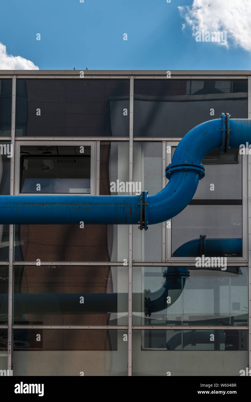 Blaue Wasserleitung vor einer Glasfassade. Stockfoto
