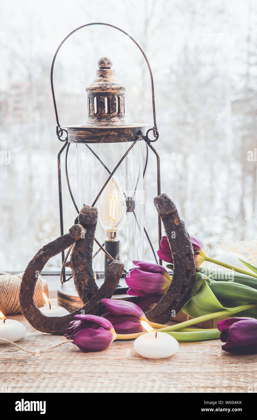 Altes rostiges Hufeisen, Braun vintage Laterne mit modernen Dimmbar dekorative Lampe auf und weiße Kerzen leuchtet und Tulpen auf Holz- Fenster Stockfoto