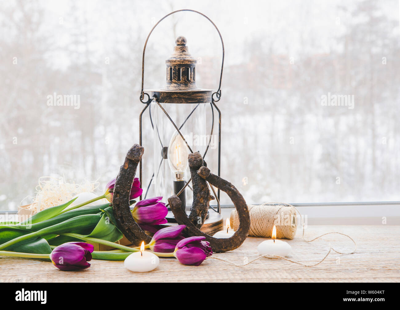 Altes rostiges Hufeisen, Braun vintage Laterne mit modernen Dimmbar dekorative Lampe auf und weiße Kerzen leuchtet und Tulpen auf Holz- Fenster Stockfoto