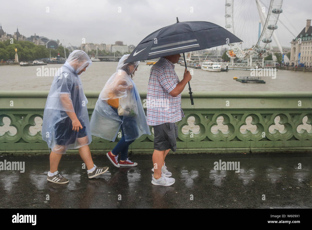 Fußgänger auf die Westminster Bridge mit Regen Ponchos und ein Schirm im regen Duschen wie ein Monat Niederschlag wurde in drei Stunden mit dem Risiko von Überschwemmungen in einigen Gebieten des Vereinigten Königreichs erwartet. Stockfoto