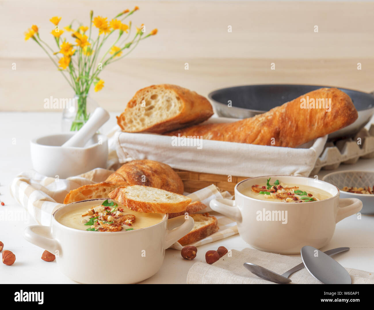 Weiße Holztisch mit 2 Schalen von Blumenkohl Suppe mit zerquetschte Haselnüsse, roter Pfeffer, glatte Petersilie Kräuter verschönert, Schweizer twisted Brot, braten Stockfoto