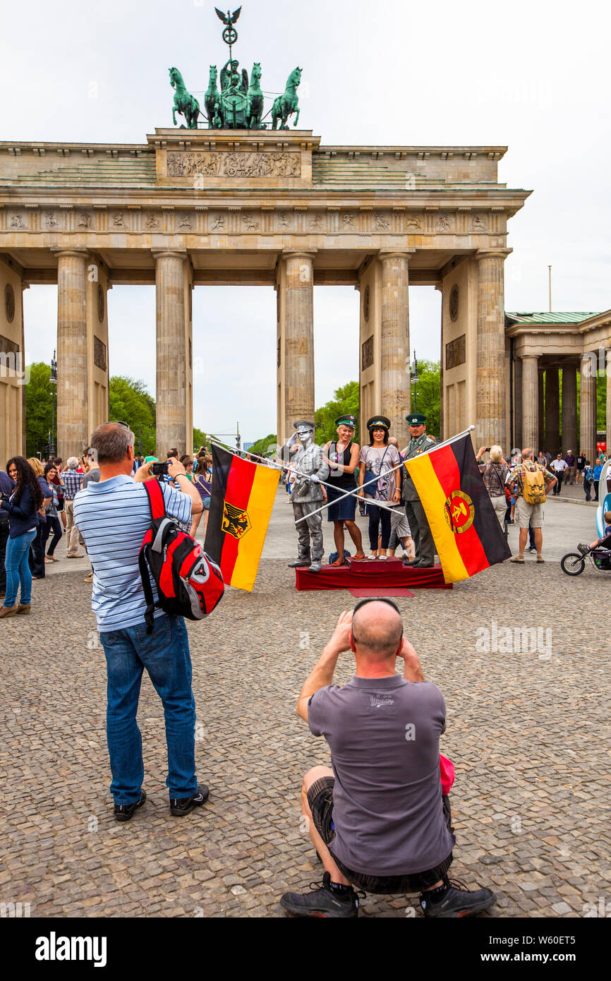 Touristen posieren mit Uniformen vor dem Brandenburger Tor, Berlin, mit den Flaggen von Ost- und Westdeutschland. Stockfoto